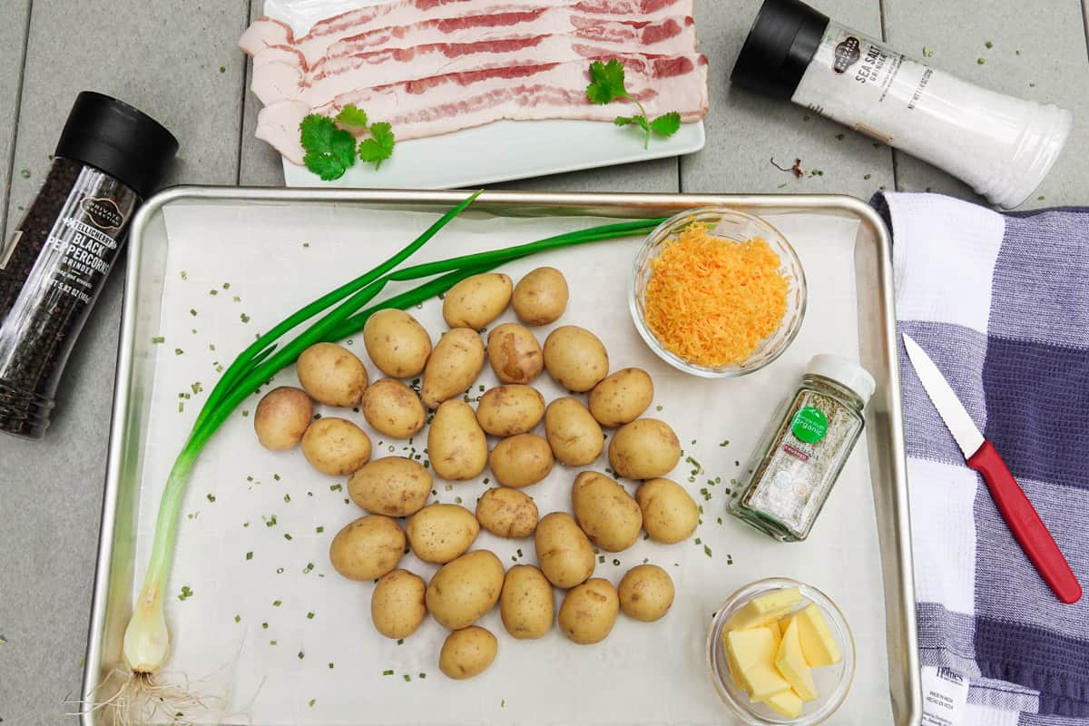 Petite gold potatoes on baking sheet with bacon, green onion, butter, and cheese surrounding the dish