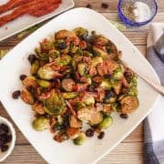 Cooked brussel sprouts on white plate topped with bacon and cranberries.