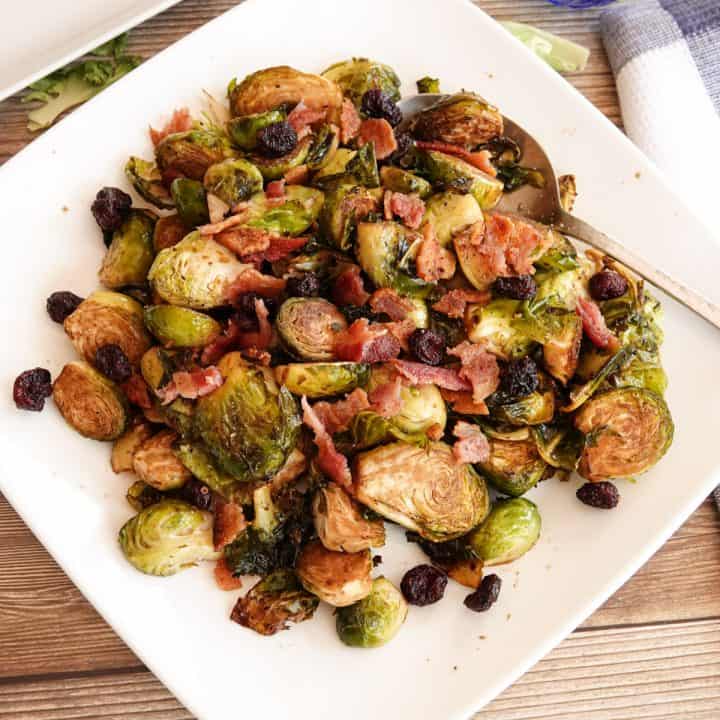 Smoked brussel sprouts on a white plate topped with bacon and cranberries