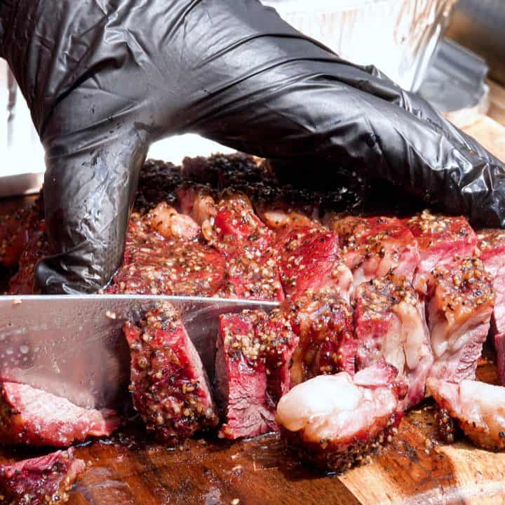 Slicing burnt ends with knife and holding meat with black glove