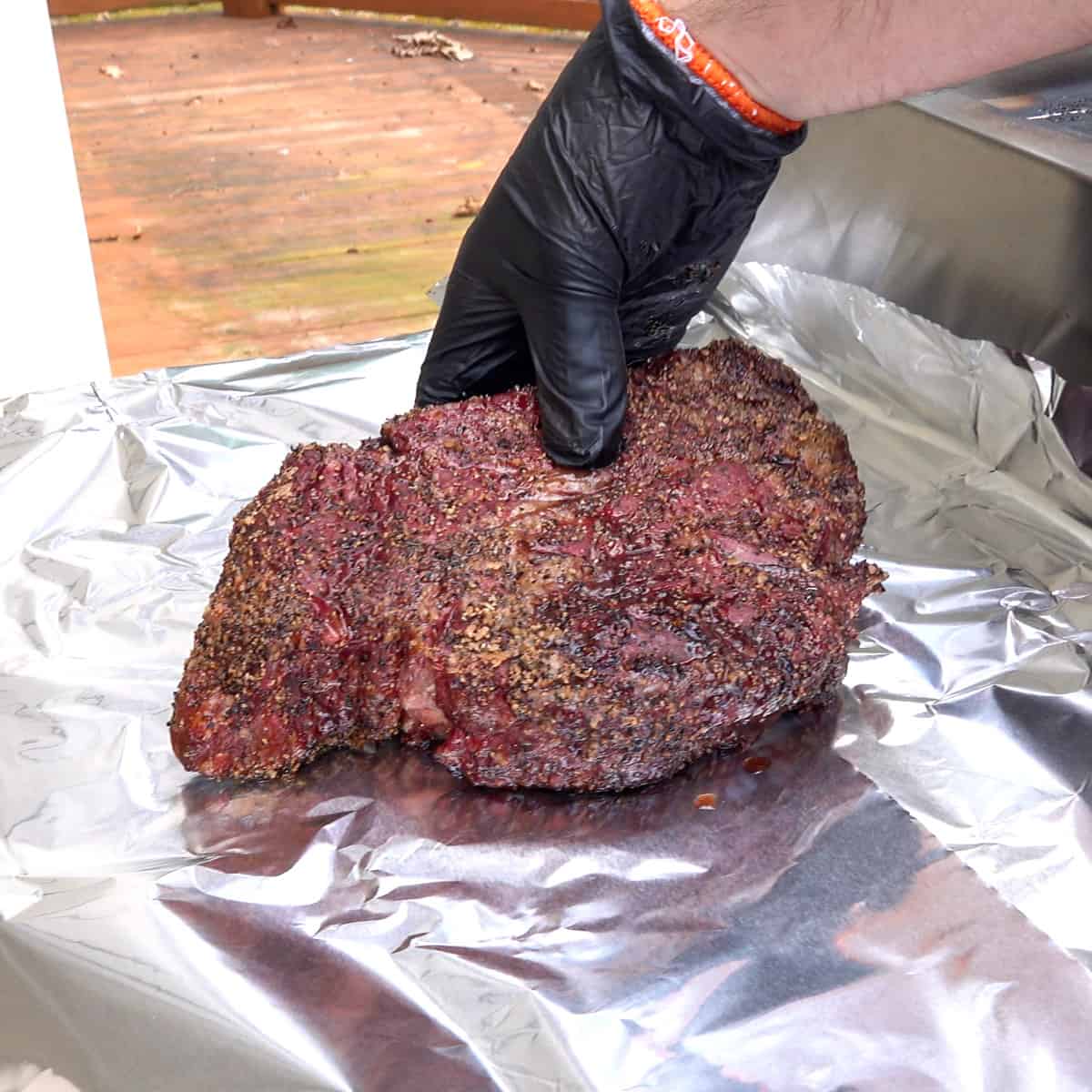 Smoked chuck roast being placed on aluminum foil