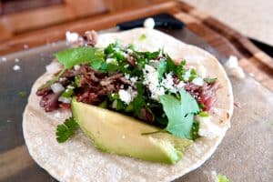 shredded pork taco, topped with chopped onion, crumbled white cheese and a slice of avocado