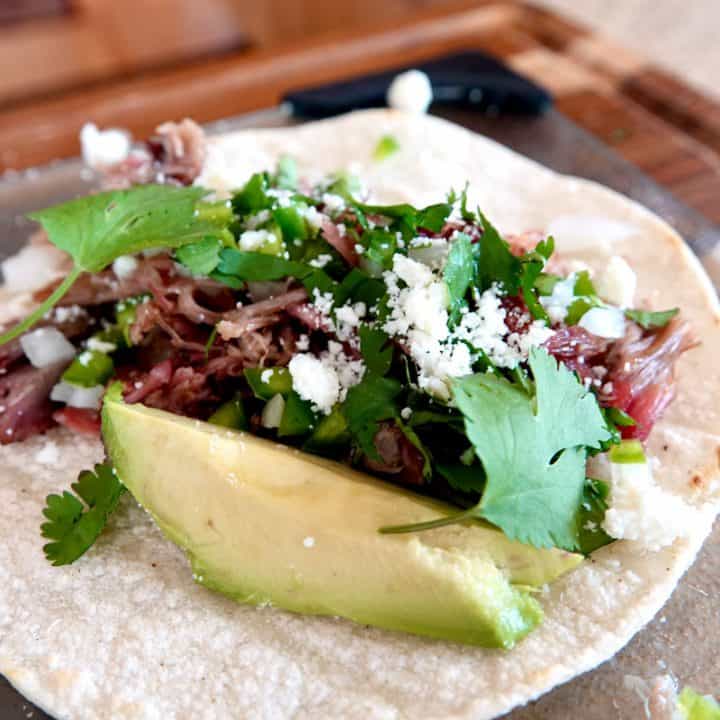 shredded pork taco, topped with chopped onion, crumbled white cheese and a slice of avocado