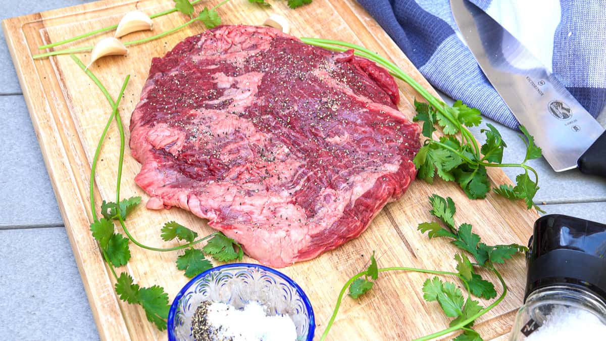 Flank steak on cutting board covered in salt and pepper