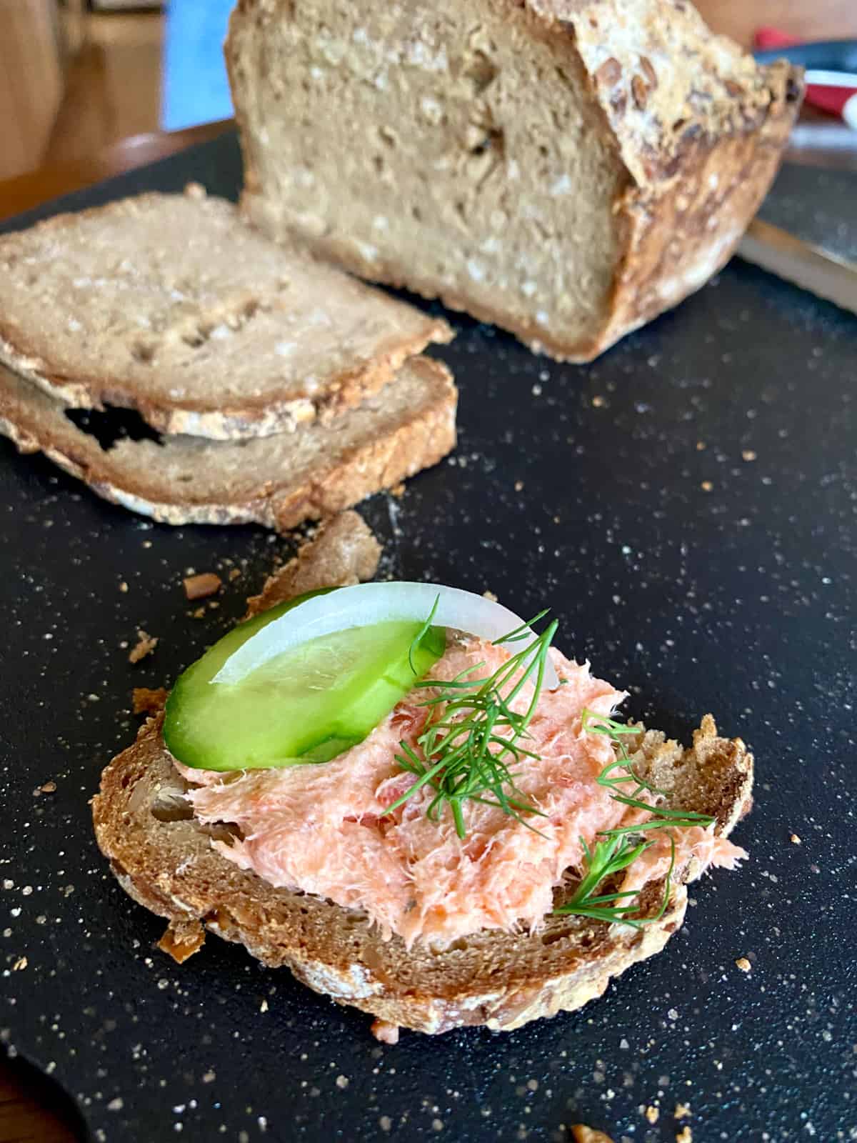 smoked salmon dip on seeded bread with slice of cucumber, onion, and dill
