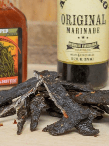 Elk jerky with a bottle of marinade and a bottle of hot sauce in background.