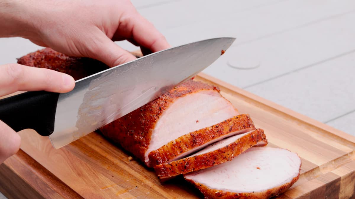 Slicing pork loin on cutting board with sharp knife