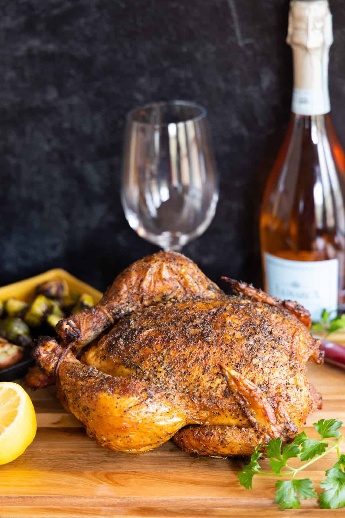 Smoked chicken on cutting board with lemons and parsley with wine bottle and glass in background