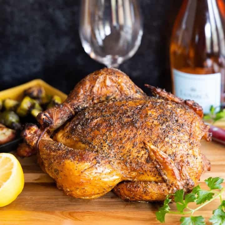 Smoked whole chicken on cutting board with lemon and bottle of wine in background.