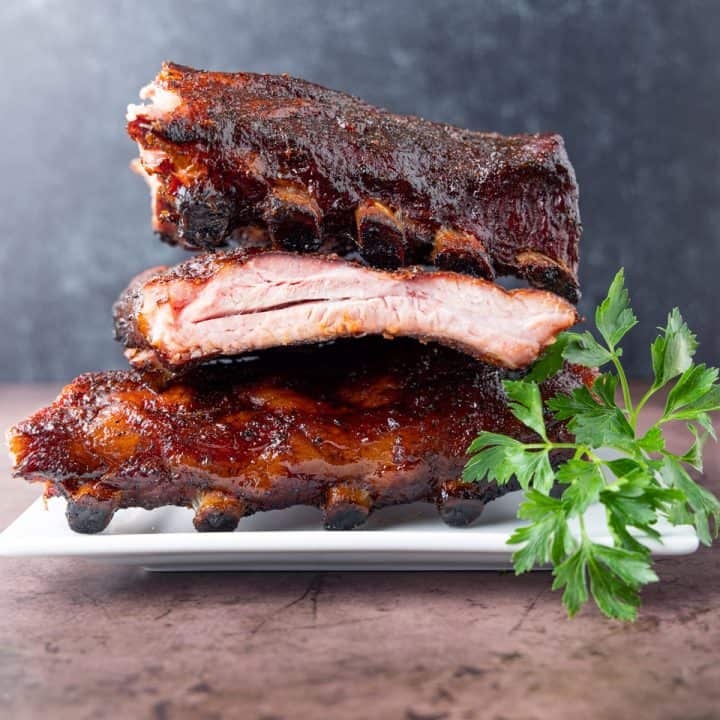 Pork ribs stacked three racks high on a white plate with green garnish.