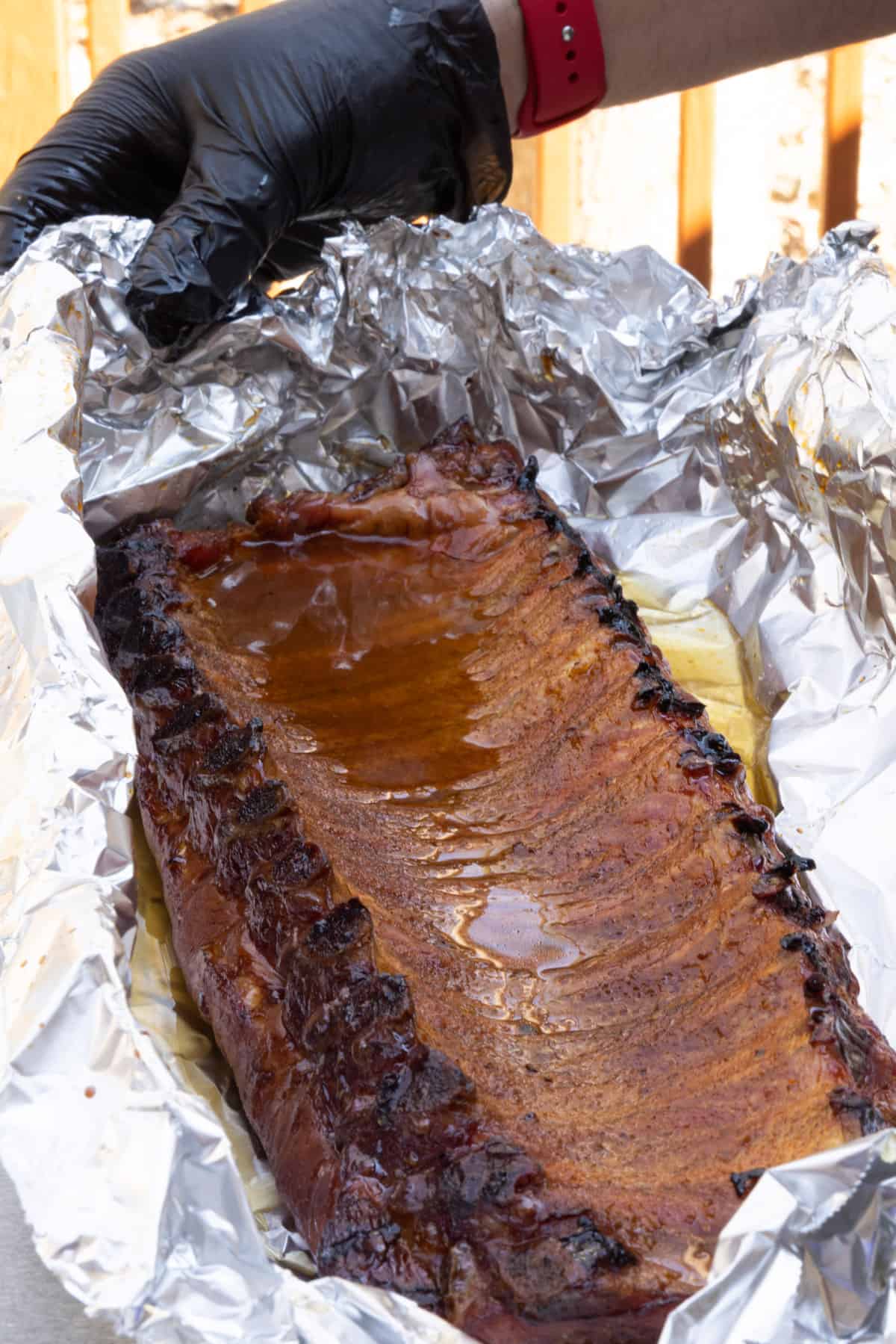 Rack of pork ribs inside a large piece of aluminum foil with liquid poured over ribs.