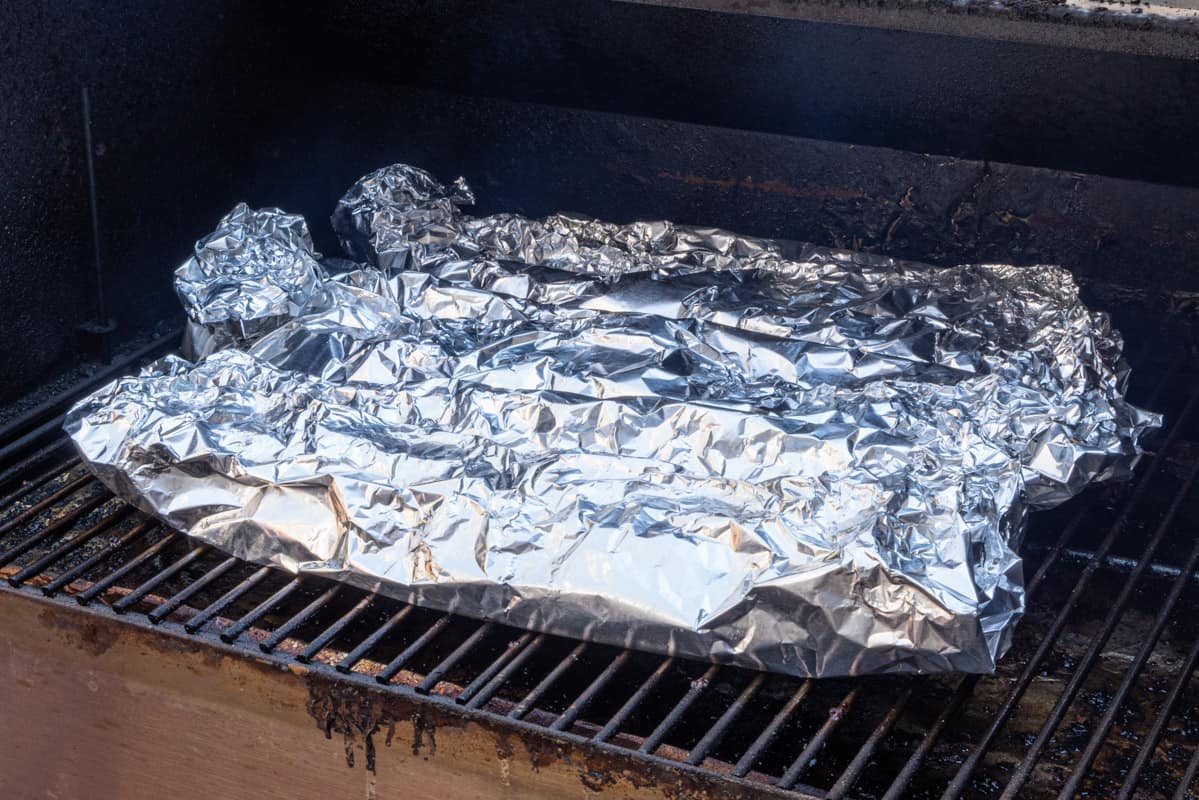 Three racks of pork ribs individually wrapped in aluminum foil and sitting on rack of smoker.
