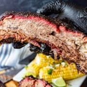 beef rib held in hand with mexican corn on the cob in background.