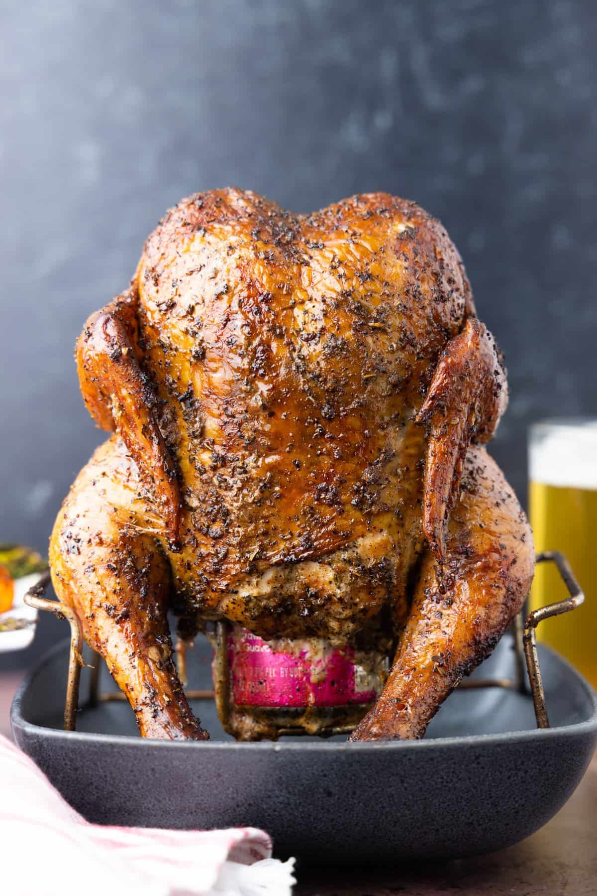 Beer can chicken on rack with black background and beer in glass