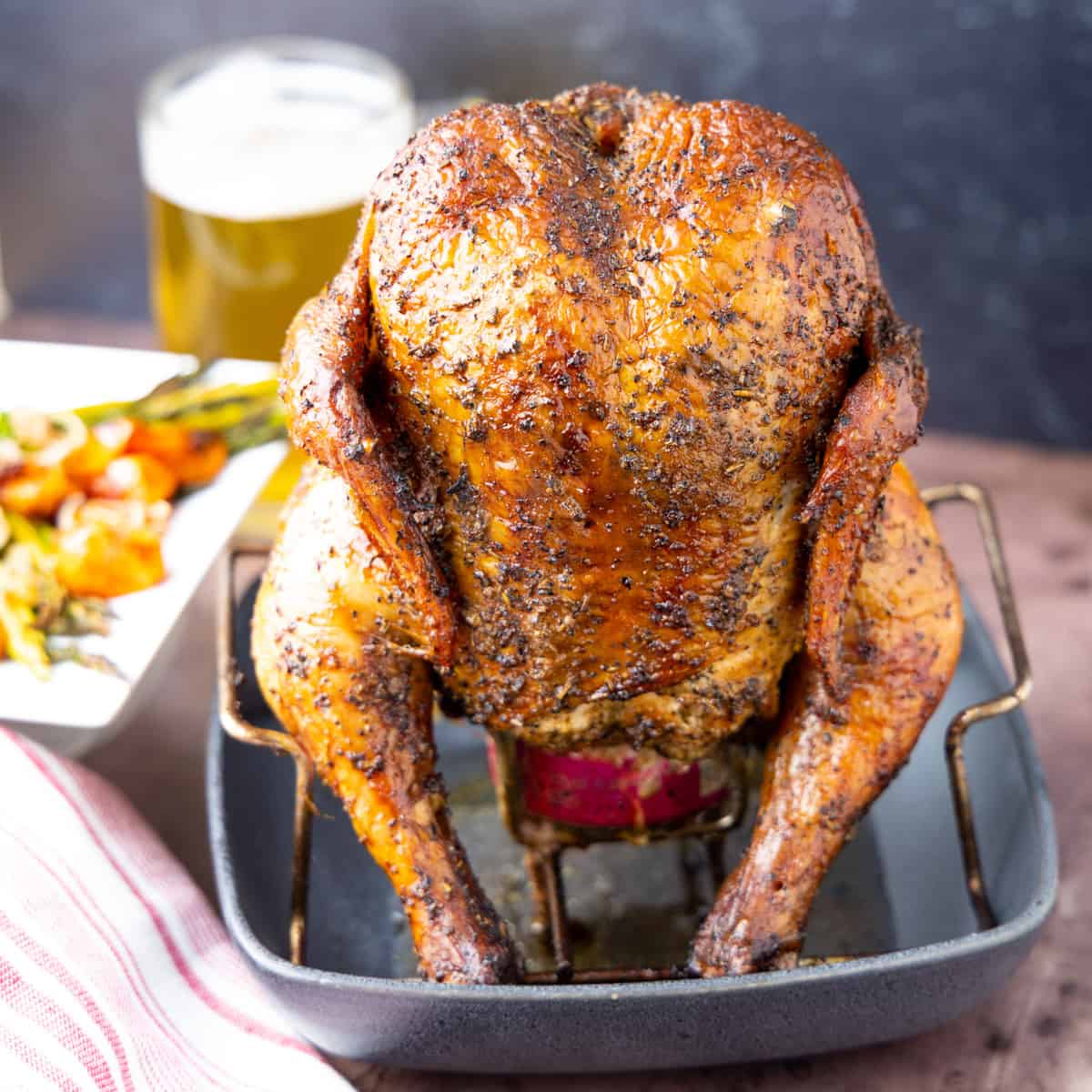 Beer can chicken in pan with beer in background.