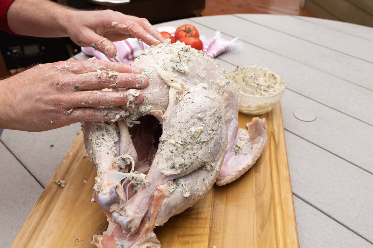 Seasoning a turkey on a cutting board with seasoned butter with mans hands. 