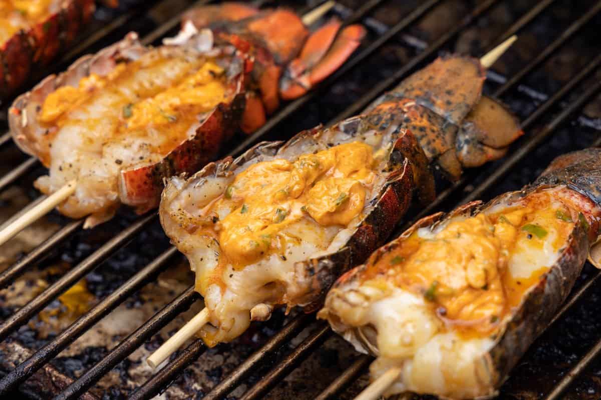 Lobster tails buttered on grill with wooden skewer stuck through tail.