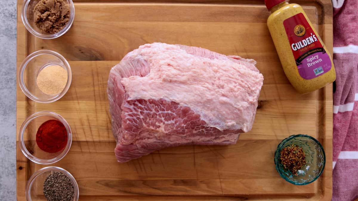 Raw corned beef brisket on cutting board with seasonings in cups.