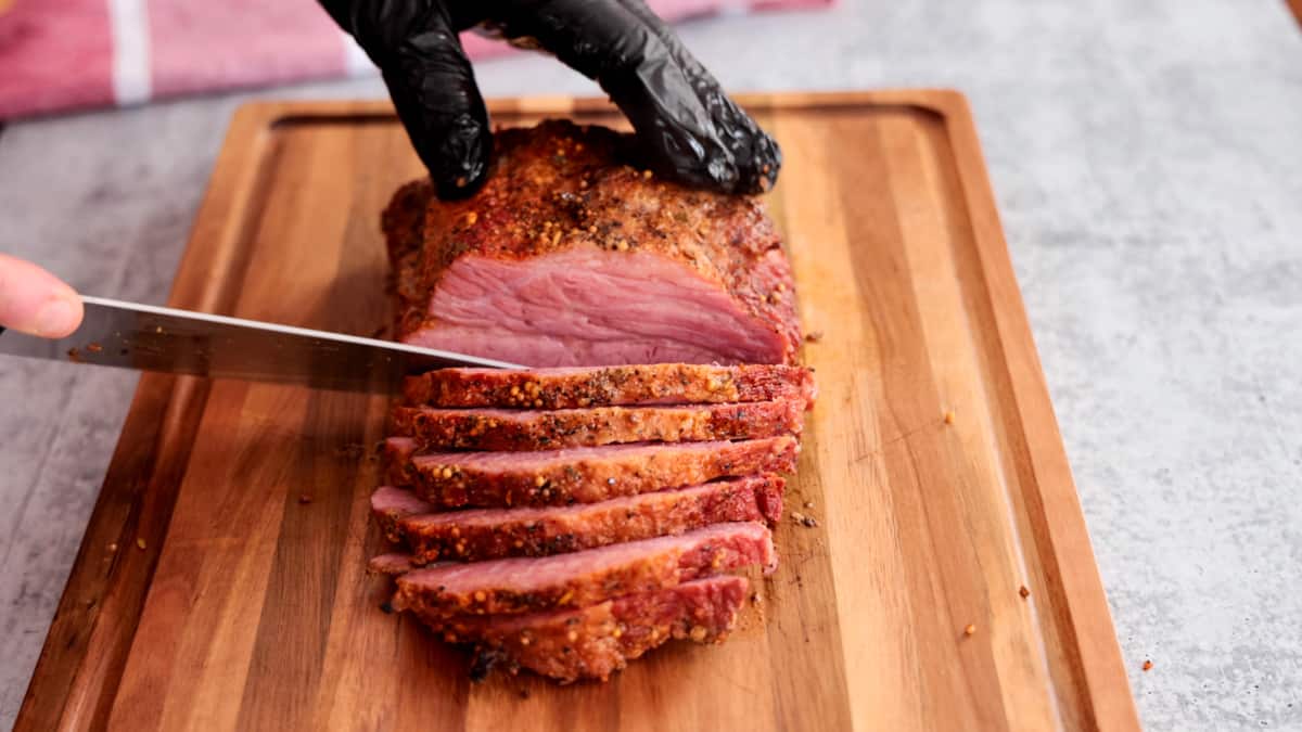Smoked corned beef being sliced on cutting board with knife.