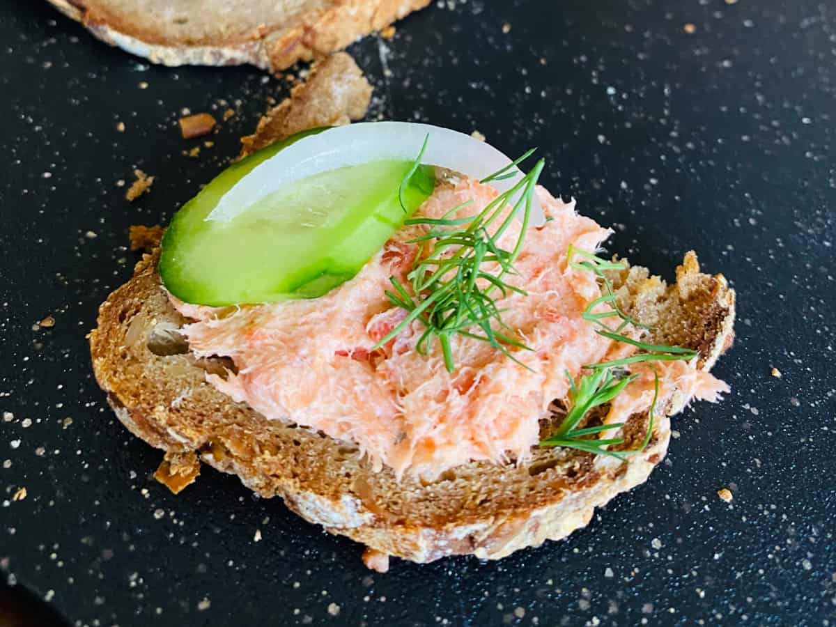 Salmon dip on toast with cucumber and black background.
