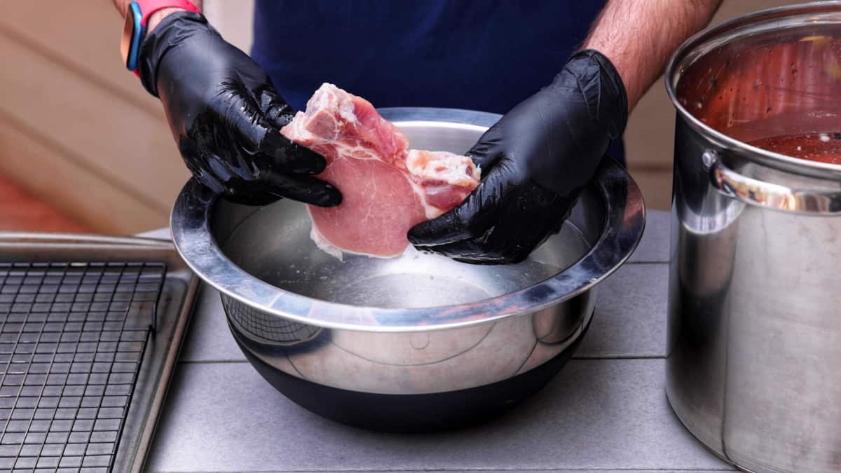 Rinsing pork chop in silver bowl of water after brining.