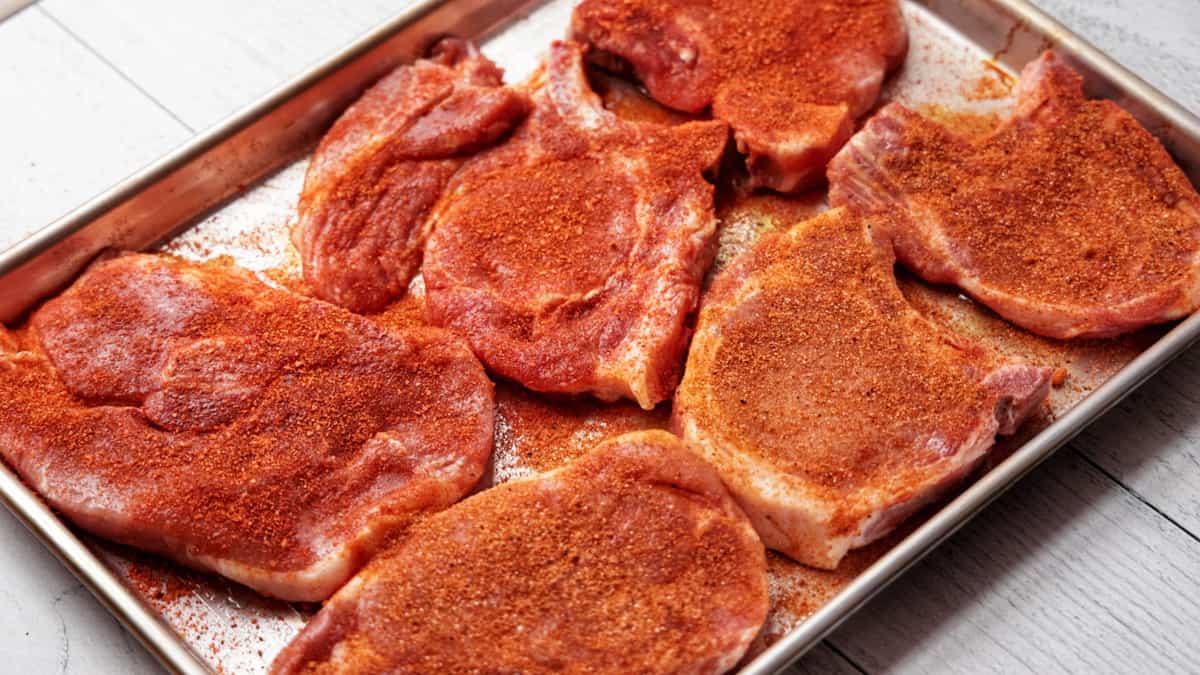 Six pork chops on baking tray seasoned for cooking