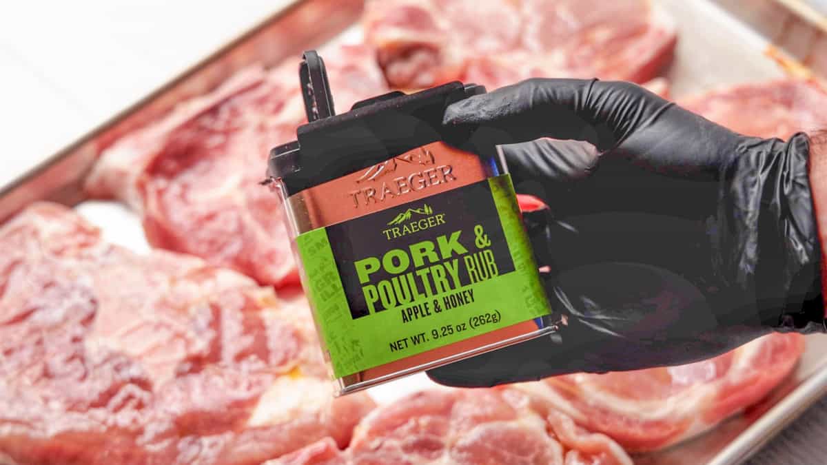 Hand in black latex glove holding Traeger pork seasoning can with pork chops in background.