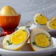 Boiled and smoked eggs cut in half on white dishes with a whole egg in a red dish.