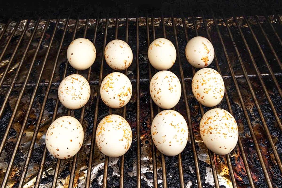 Twelve eggs on grill, smoking until fully cooked.