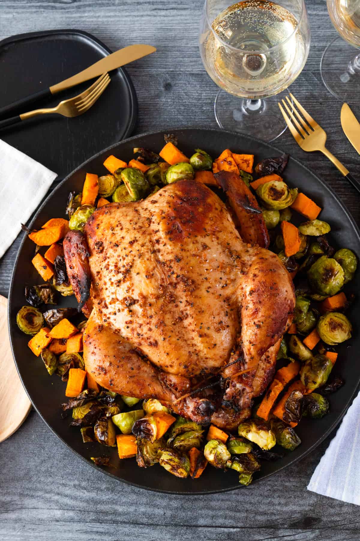 Smoked chicken on dark platter with vegetables surrounding chicken.