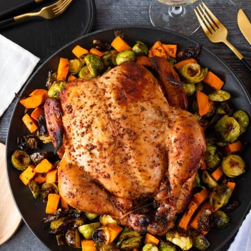 Smoked chicken surrounded by vegetables on dark platter.