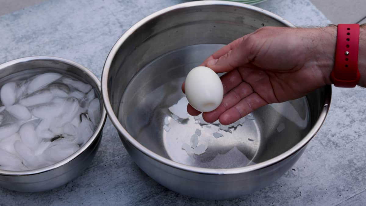 Holding a peeled egg over a bowl full of water.