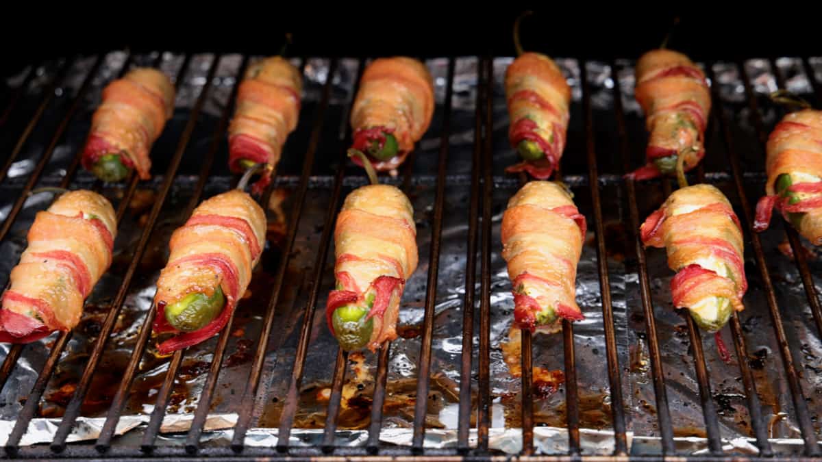 A dozen bacon wrapped jalapeno poppers on grill cooking.