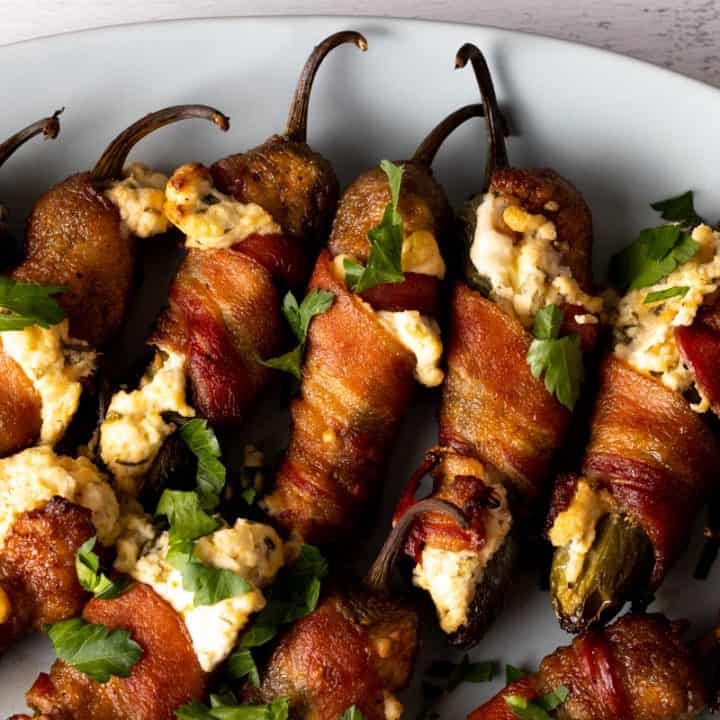 Cooked cream cheese stuffed bacon wrapped jalapenos on white plate.