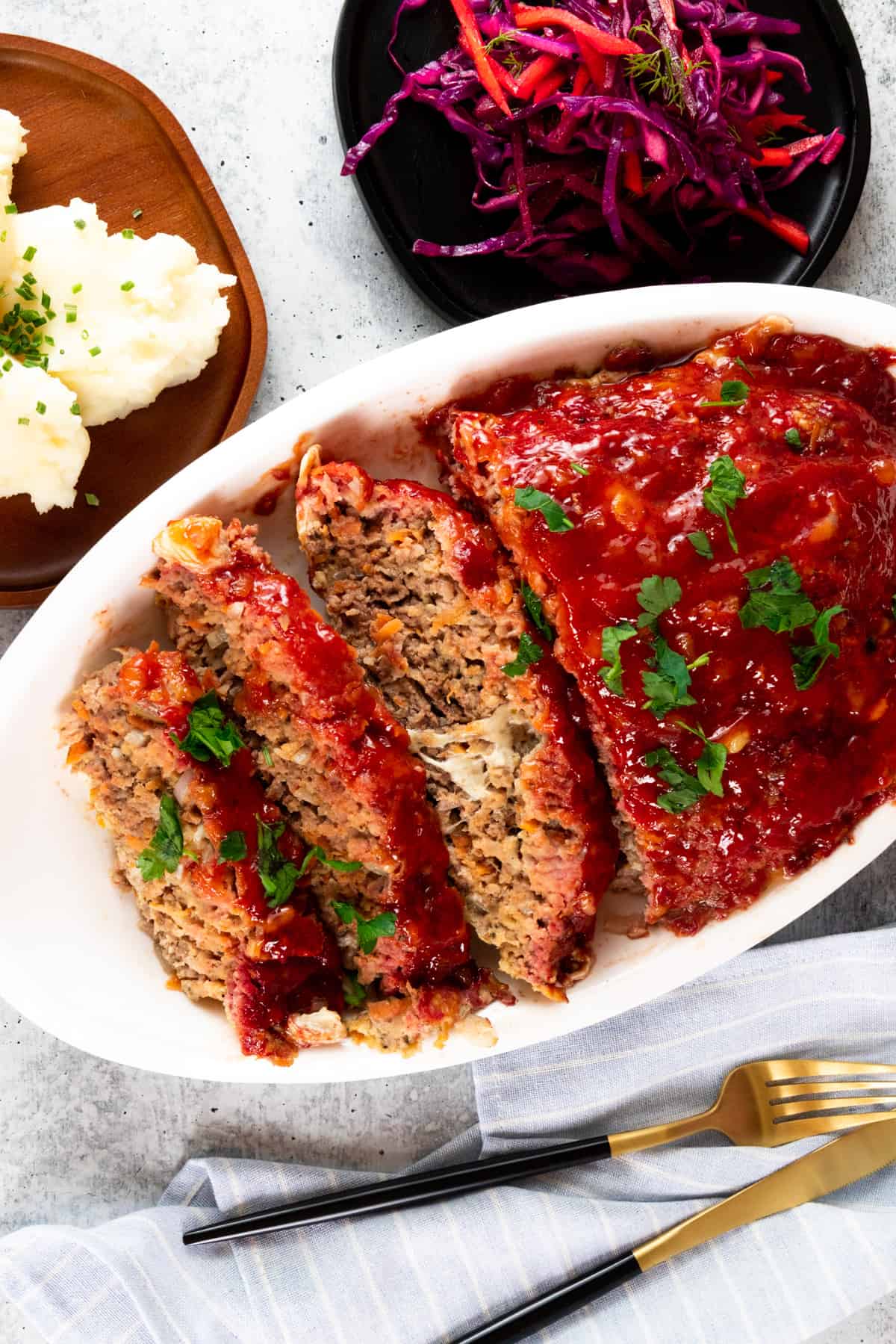 meatloaf in white platter with knife and fork along with cabbage on the side.