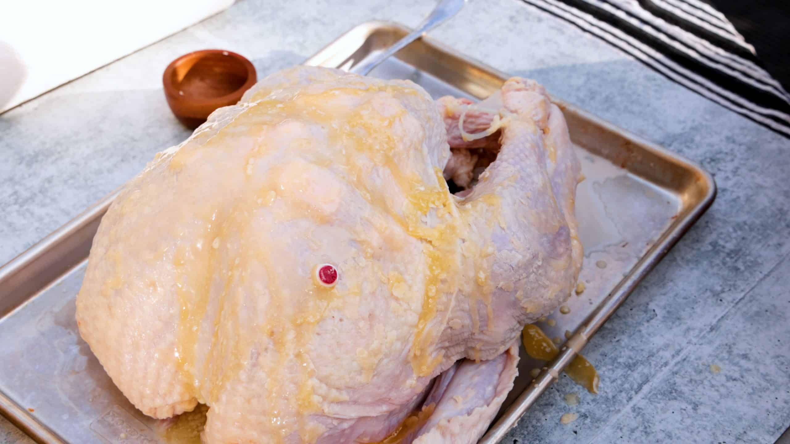 Uncooked raw turkey on baking sheet drizzled with melted butter.