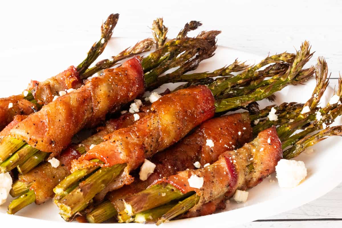 Bacon wrapped around asparagus topped with blue cheese on white plate.
