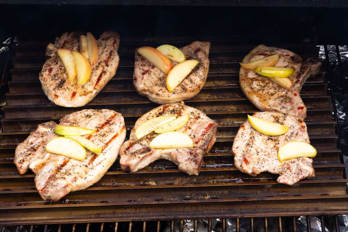 Pork chops topped with apple slices on searing rack on grill. 