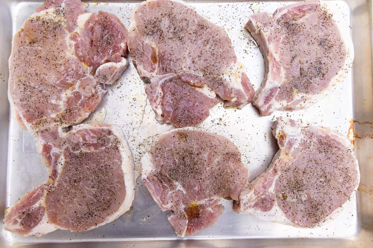 Pork chops laying on paper towels and seasoned with spices in preparation to grill. 