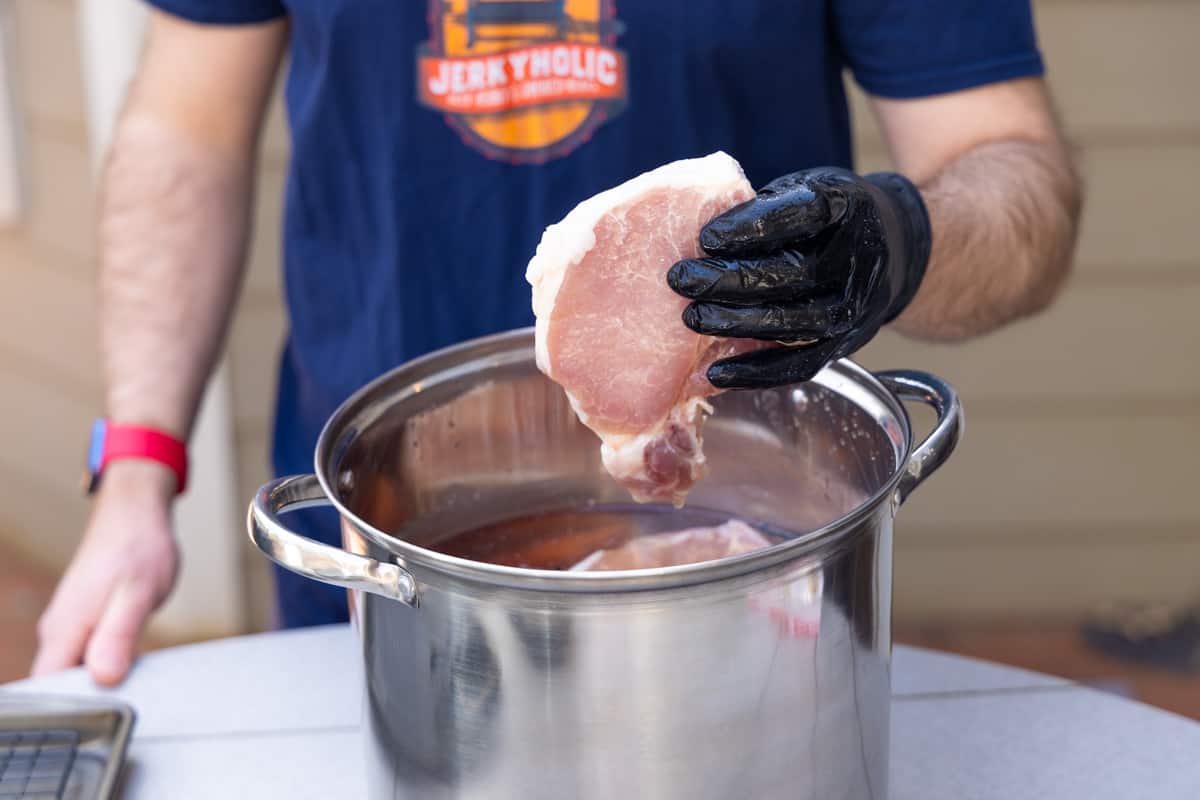 Man removing pork chops from water brine in silver pot.