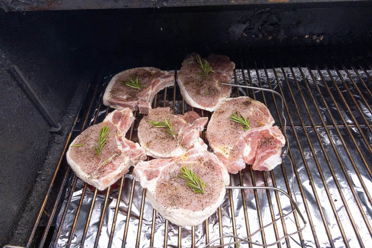 Pork on grill grates topped with rosemary, cooking.