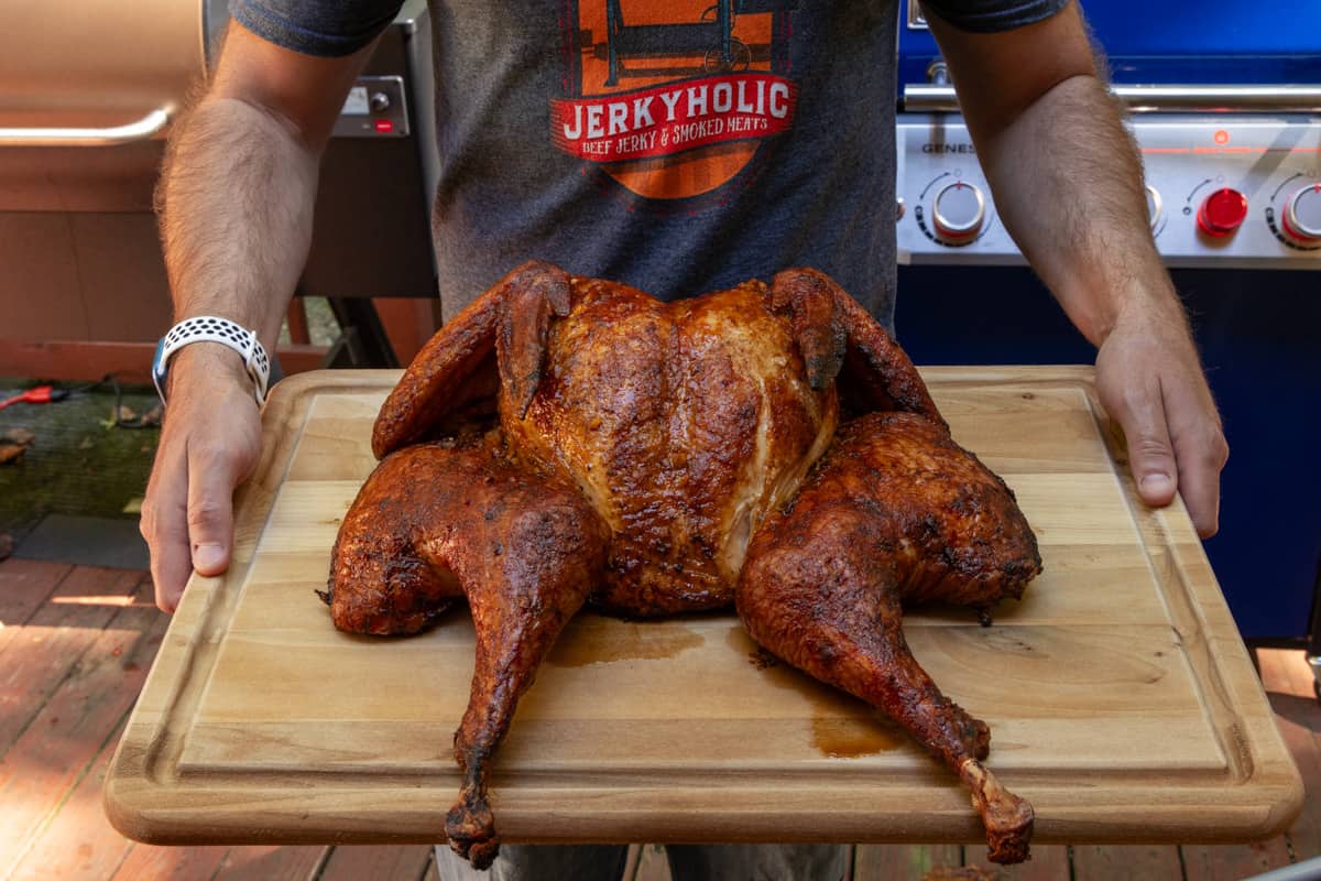 Spatchcock turkey on cutting board after cooking being held by man wearing a jerkyholic t shirt.