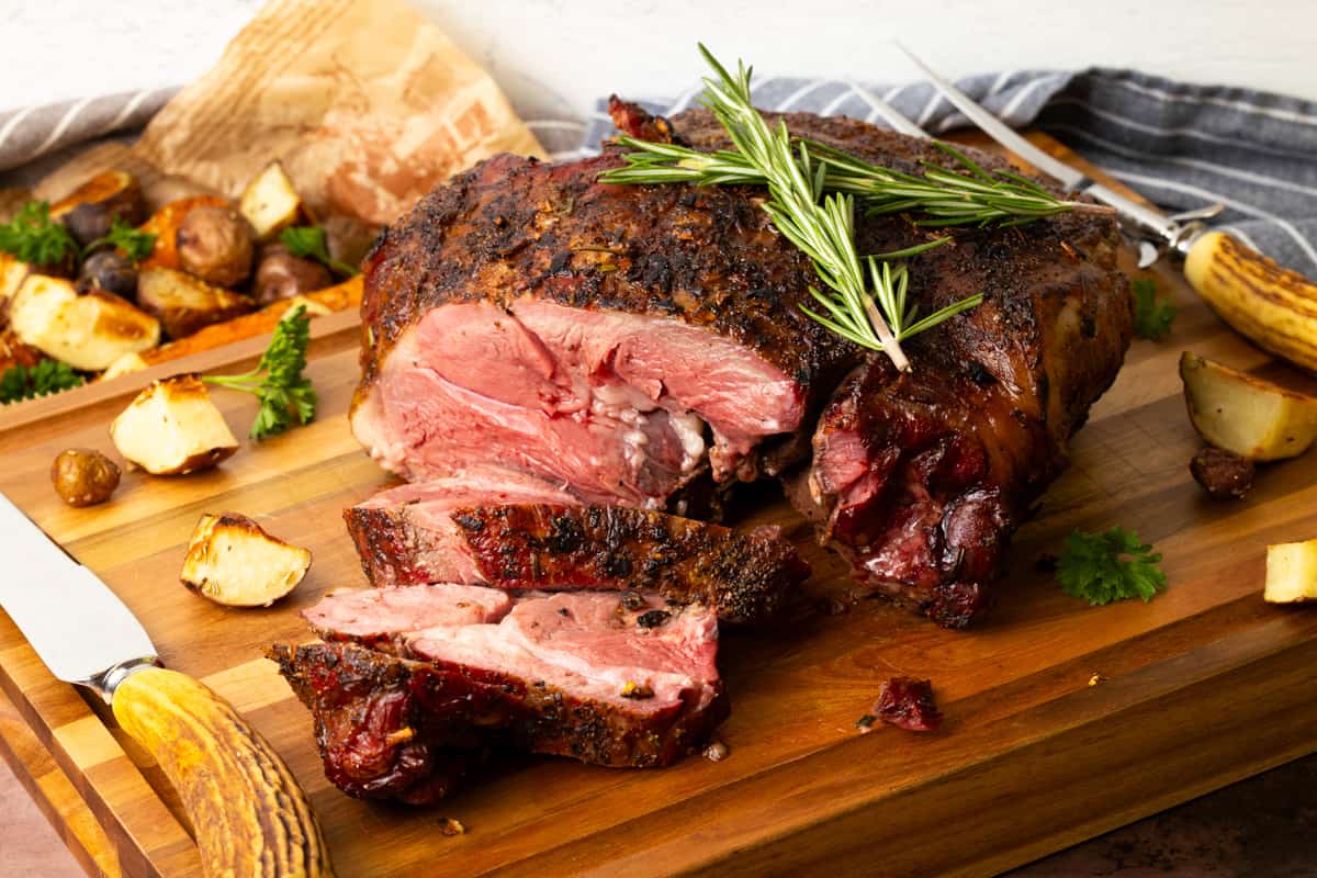 Sliced leg of lamb on cutting board topped with rosemary.