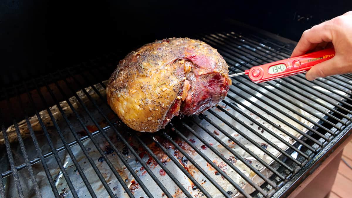 Testing the temperature of a lamb roast with red meat thermometer on grill.