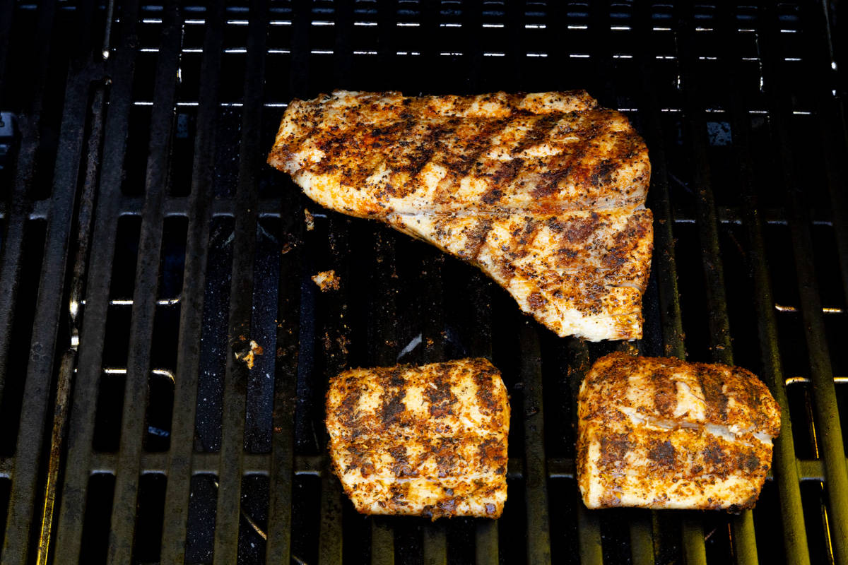 Three grilled fish fillets on grill.