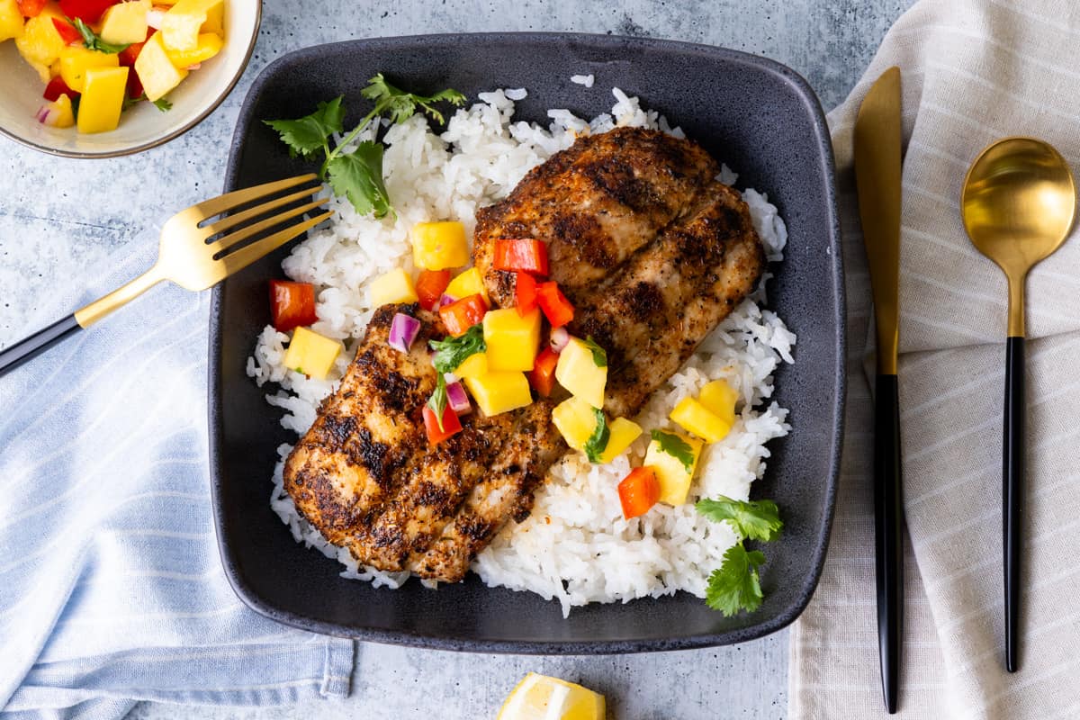 Mahi fish atop rice topped with mango salsa in a blue square bowl.