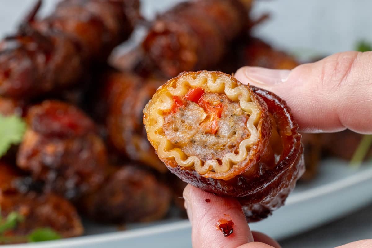 Two fingers holding a stuffed pasta shotgun shell up close showing the meat filling.