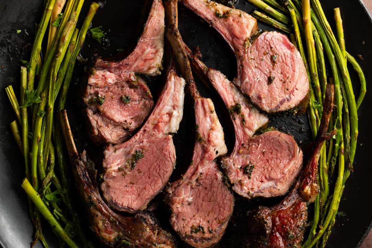 Five lamb chops on black platter surrounded by grilled asparagus.