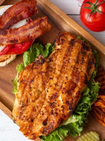 Grilled chicken breast on a bed of lettuce atop a wooden platter.