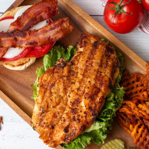 Grilled chicken breast on a bed of lettuce atop a wooden platter.